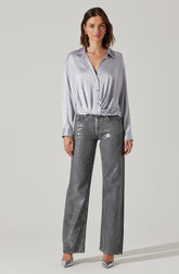 A woman is wearing a light silver, long-sleeved, button-up shirt with a collar. The shirt has a slightly shiny, satin-like texture and is tucked into high-waisted, wide-leg gray jeans with a metallic sheen. She is also wearing pointed-toe heels with a metallic finish.